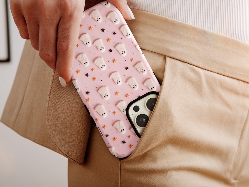 May include: A pink phone case with a pattern of white ghosts and orange stars. The case is in someone's pocket.