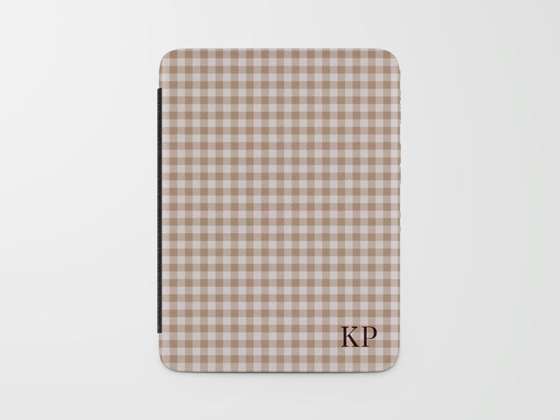 May include: A tan and white gingham pattern tablet case with the initials "KP" in the lower right corner. The case has a black spine and a rounded top edge.