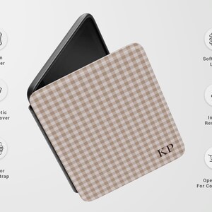 May include: A phone case with a tan and white gingham pattern. The case has a magnetic front cover, interior hand strap, and is impact resistant. The case is made of vegan leather and has a soft fabric liner. The initials "KP" are visible.