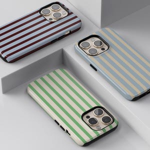May include: Three smartphone cases with striped patterns. One case has blue and brown stripes, another has blue and beige stripes, and the third has green and white stripes. The cases have a glossy finish and a black border.