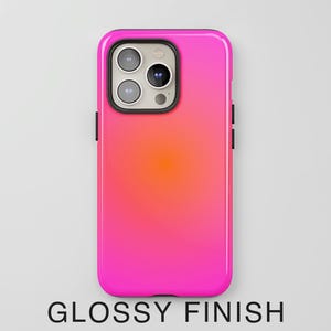 May include: A glossy phone case with a gradient design, transitioning from bright pink to orange. The case has a black border and features the camera module. The text "GLOSSY FINISH" is at the bottom.