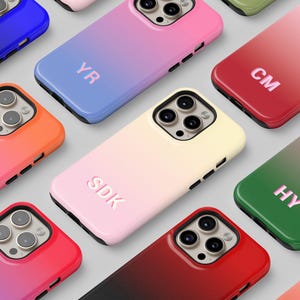 May include: A collection of colorful phone cases with a gradient design. Each case features a unique color combination, such as pink to red, blue to purple, and green to pink. Some cases have initials embossed on them.