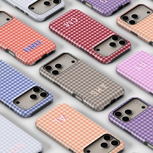 May include: A collection of phone cases with a gingham pattern in various colors, including red, blue, pink, and purple. Each case features a personalized monogram in a contrasting color. The cases are designed to fit a smartphone.