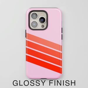 May include: A light pink smartphone case with a glossy finish, featuring three diagonal stripes in varying shades of orange and red across the lower portion. The case has a black camera cutout housing three circular lenses and a flash.