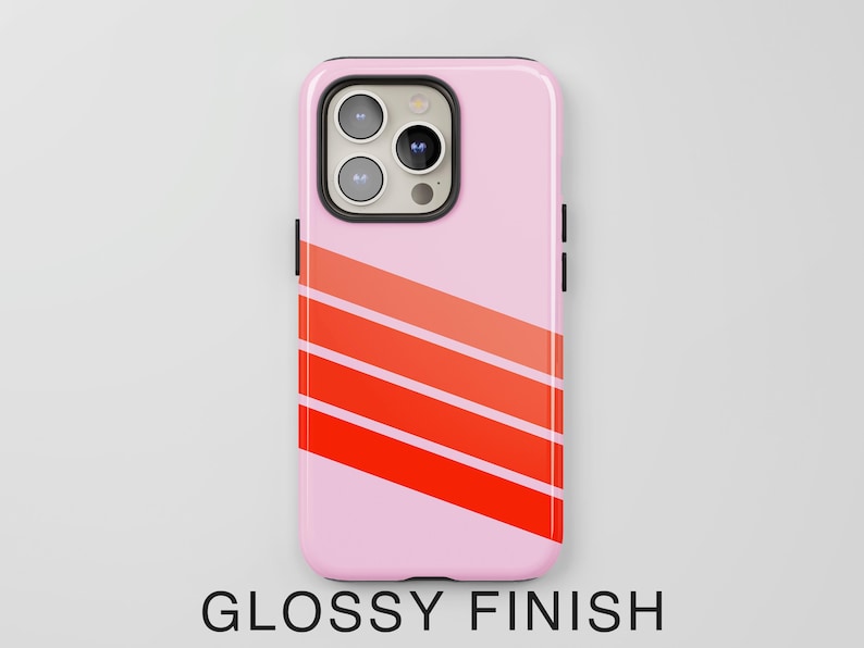 May include: A light pink smartphone case with a glossy finish, featuring three diagonal stripes in varying shades of orange and red across the lower portion. The case has a black camera cutout housing three circular lenses and a flash.