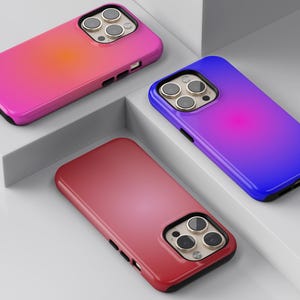 May include: Three smartphone cases in vibrant colors: pink, red, and blue, each with a gradient effect. The cases have a black border and a camera cutout with three lenses.