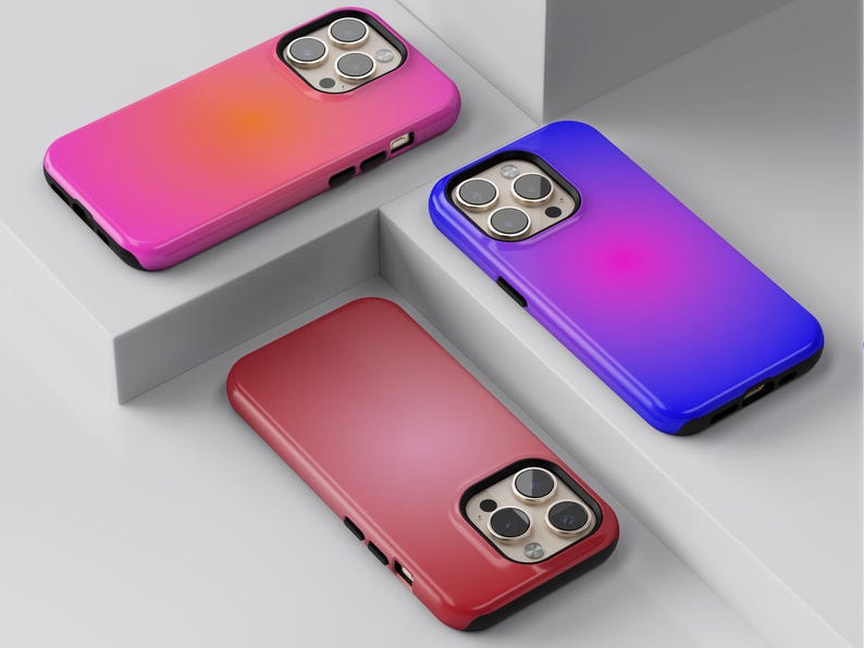 May include: Three smartphone cases in vibrant colors: pink, red, and blue, each with a gradient effect. The cases have a black border and a camera cutout with three lenses.