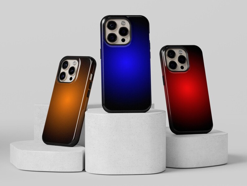 May include: Three smartphone cases with a gradient design. One case has an orange to brown gradient, another has a blue to black gradient, and the third has a red to black gradient. The cases are on white pedestals.