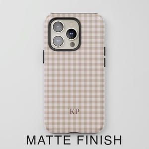 Puede incluir: Una funda para tel&eacute;fono con un patr&oacute;n de cuadros vichy en beige y blanco y acabado mate. La funda presenta un recorte para triple c&aacute;mara en la parte superior izquierda y las letras KP impresas en una fuente serif oscura en la parte inferior.