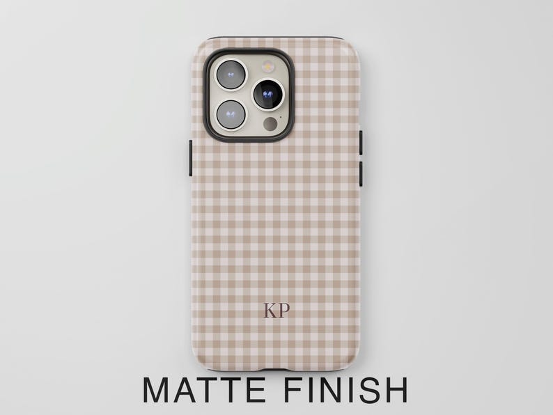Puede incluir: Una funda para tel&eacute;fono con un patr&oacute;n de cuadros vichy en beige y blanco y acabado mate. La funda presenta un recorte para triple c&aacute;mara en la parte superior izquierda y las letras KP impresas en una fuente serif oscura en la parte inferior.