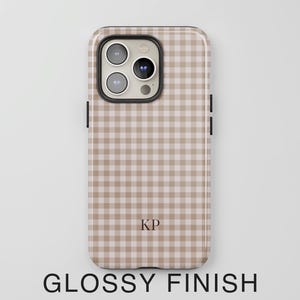 Puede incluir: Una funda para smartphone con acabado brillante que presenta un patr&oacute;n de cuadros vichy en color beige claro y blanco. La funda incluye un recorte para la c&aacute;mara con tres lentes y un flash. Las letras KP est&aacute;n impresas en la parte inferior central.