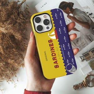 May include: A yellow phone case with a blue and white sardine can design. The can says "Original Sardines In Olive Oil Traditional Recipe".