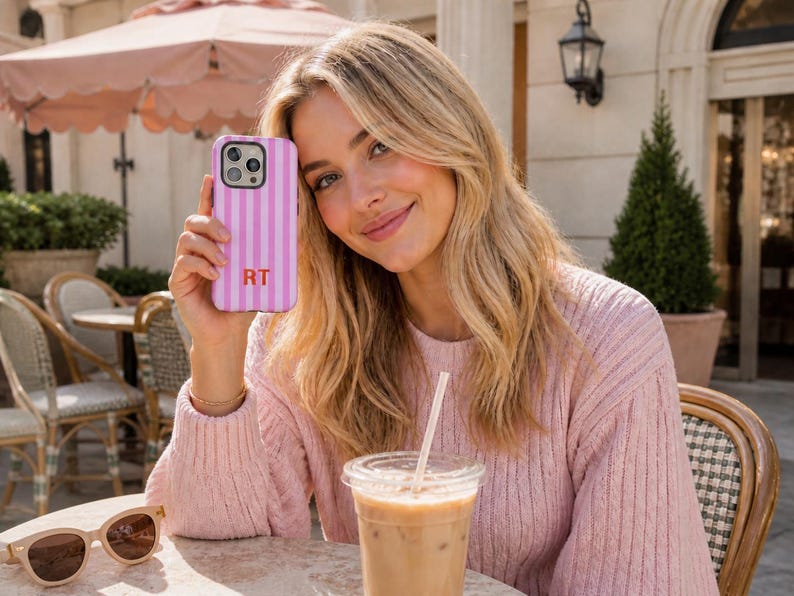 May include: A pink and white vertically striped smartphone case featuring the letters RT in a bold orange font. The case has a cutout for a triple-lens camera system and is designed to fit a modern smartphone with a sleek, protective exterior.