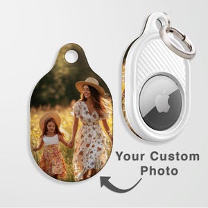 May include: Custom photo keychain with a picture of a woman and child in a field. The keychain is oval-shaped with a hole at the top. A white AirTag with a silver ring is also shown. Text reads "Your Custom Photo".