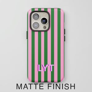 May include: A smartphone case with a matte finish featuring vertical pink and green stripes. The center of the case displays the letters LYT in a purple font with a slight shadow effect. The case has a cutout for a triple-lens camera system.
