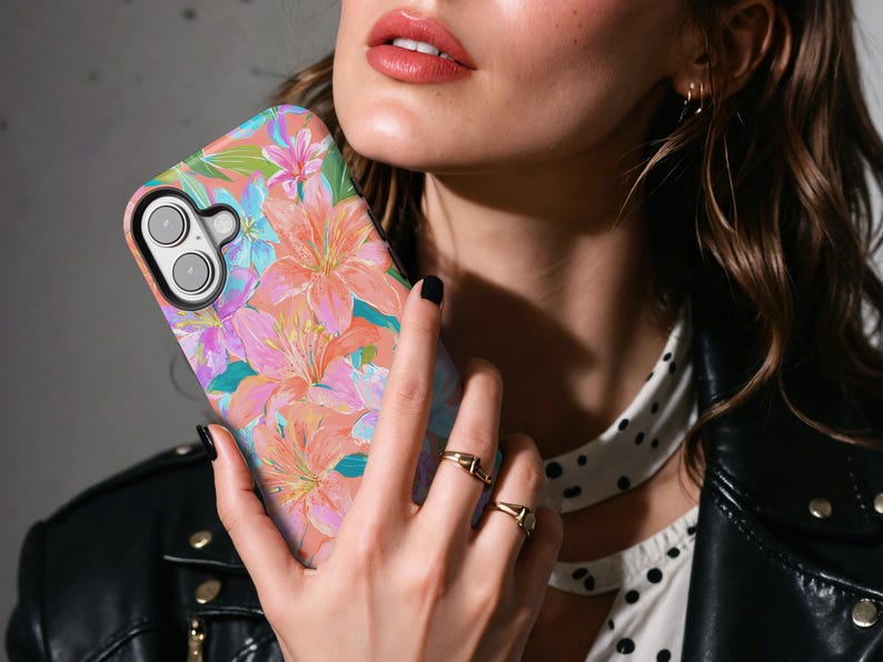 May include: A floral phone case featuring a vibrant design of pink, orange, and blue lilies. The case has a glossy finish and a black camera module. The overall theme is nature and art.