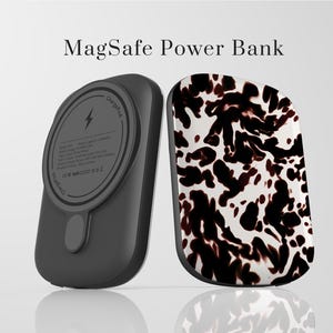 Puede incluir: Dos baterías externas MagSafe. Una es negra con una plataforma de carga y la otra tiene un patrón de manchas blancas y marrones. El texto "MagSafe Power Bank" está en la parte superior de la imagen.