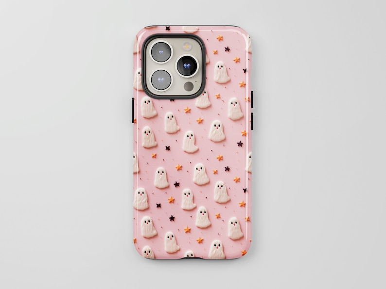 May include: A pink phone case featuring a pattern of white ghosts and orange stars. The case is designed for a phone with a camera bump.