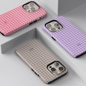 Puede incluir: Tres fundas para smartphone con un patr&oacute;n de cuadros vichy en rosa, morado y beige. Cada funda tiene un recorte para triple c&aacute;mara y un monograma personalizado de dos letras impreso en la parte posterior, con bordes negros.