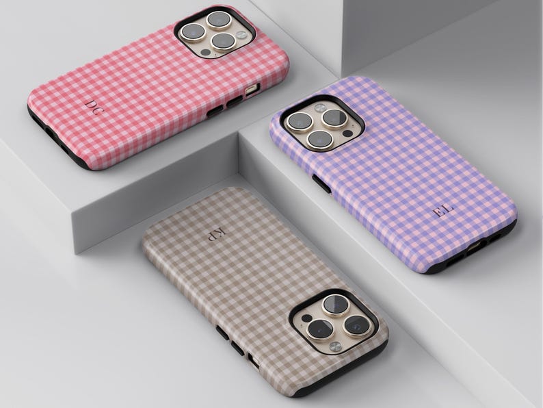 Puede incluir: Tres fundas para smartphone con un patr&oacute;n de cuadros vichy en rosa, morado y beige. Cada funda tiene un recorte para triple c&aacute;mara y un monograma personalizado de dos letras impreso en la parte posterior, con bordes negros.
