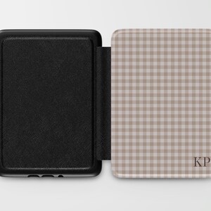 May include: Black protective case for an e-reader, open to reveal a tan and white gingham pattern. The case has a textured black exterior and the interior features the initials "KP".