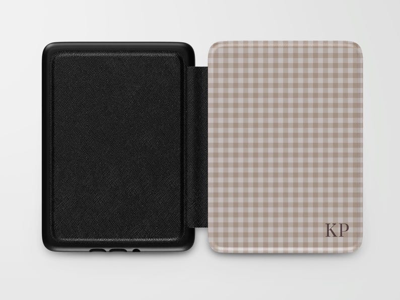 May include: Black protective case for an e-reader, open to reveal a tan and white gingham pattern. The case has a textured black exterior and the interior features the initials "KP".