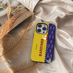 May include: A yellow and blue phone case with a sardine can design. The case features the text "ORIGINAL SARDINES" and a traditional recipe label. The case has a blue background with white fish silhouettes.