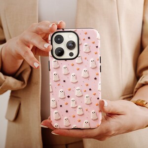 May include: A pink phone case with a pattern of white ghosts and orange stars. The case is designed for an iPhone.