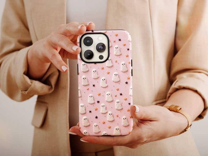 May include: A pink phone case with a pattern of white ghosts and orange stars. The case is designed for an iPhone.