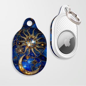 May include: A white AirTag holder with a blue and gold sun and moon design. The holder has a key ring attached.