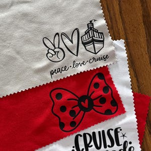 May include: Three white microfiber cloths with black iron-on vinyl designs. The top cloth has a peace sign, a heart, a cruise ship, and the text "peace.love.cruise". The middle cloth has a red bow with black polka dots. The bottom cloth has an anchor, the text "cruise mode", and a power button.