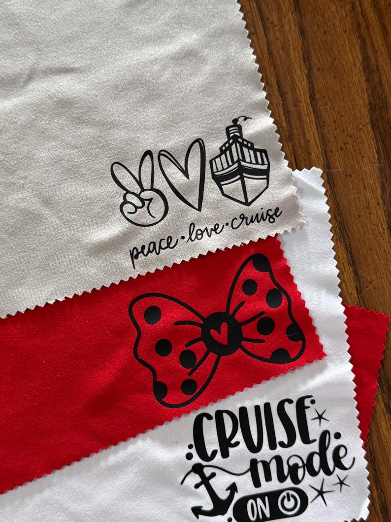 May include: Three white microfiber cloths with black iron-on vinyl designs. The top cloth has a peace sign, a heart, a cruise ship, and the text "peace.love.cruise". The middle cloth has a red bow with black polka dots. The bottom cloth has an anchor, the text "cruise mode", and a power button.