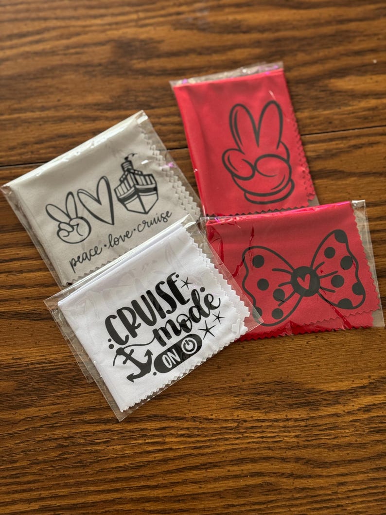 May include: Four different microfiber cleaning cloths with various designs. The cloths are packaged in clear plastic bags. The designs include a peace sign, a heart, a cruise ship, a Mickey Mouse hand, a bow, and the text "Cruise Mode On".