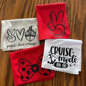 May include: Four white microfiber cloths with black printed designs. The designs include a peace sign, a heart, a cruise ship, a bow with polka dots, an anchor, and the text "cruise mode on".