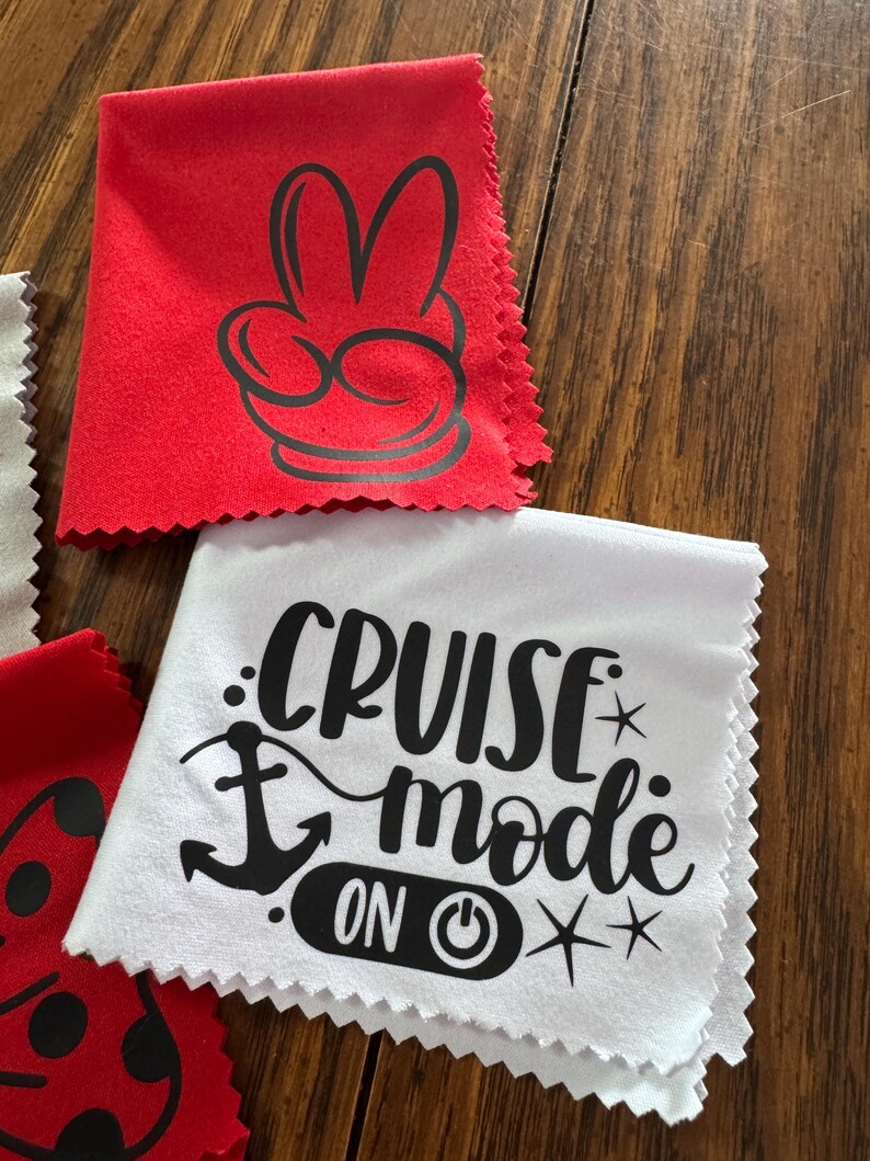 May include: Two red microfiber cloths with black designs. One cloth has a Mickey Mouse hand with two fingers up. The other cloth has a white anchor and the text "Cruise Mode On" with a power button symbol.