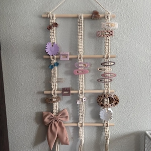 May include: A macrame wall hanging with wooden dowels and tassels, used to display hair clips and accessories. The clips are in various colors and styles, including floral, geometric, and leopard print.