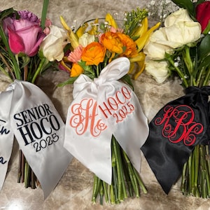 May include: Bouquets of flowers with satin ribbons. One bouquet has a white ribbon with "Austin & Alyssa" and "Senior HOCO 2025" in black. Another has a white ribbon with an orange monogram and "HOCO 2025". The last has a black ribbon with a red monogram and "HOCO 2025".