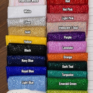 May include: A collection of rectangular fabric swatches featuring a glittery, sequined texture arranged in two columns. Colors include maroon, red, hot pink, light pink, iridescent, purple, lavender, orange, dark teal, turquoise, emerald green, lime green, iridescent white, white, silver, gold, yellow, black, navy blue, royal blue, and light blue. The text Hill Girls DESIGNS is at the bottom.