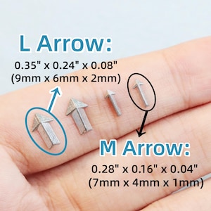 May include: Close-up of several small, silver-colored arrow charms. The image includes text that reads "L Arrow: 0.35" x 0.24" x 0.08" (9mm x 6mm x 2mm)" and "M Arrow: 0.28" x 0.16" x 0.04" (7mm x 4mm x 1mm)".