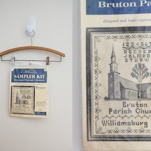 May include: A sampler kit for cross-stitching featuring a black and white illustration of Bruton Parish Church in Williamsburg, Virginia. The kit includes a pattern and instructions for stitching the church, along with the alphabet and numbers.