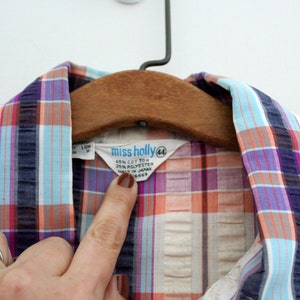 May include: A white, blue, pink, and orange plaid shirt with a "Miss Holly" label. The label says "65% Cotton 35% Polyester Made in Japan" and has a size tag that says "44".
