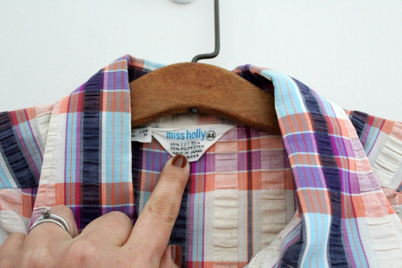 May include: A white, blue, pink, and orange plaid shirt with a "Miss Holly" label. The label says "65% Cotton 35% Polyester Made in Japan" and has a size tag that says "44".