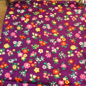 May include: Purple fabric with a small floral pattern in shades of pink, yellow, red, and green.