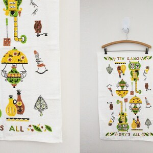 May include: White kitchen towel with a colorful retro design featuring various kitchen appliances and the text "DRY'S ALL". The towel is hanging on a wooden hanger against a white wall. The design includes yellow, green, and brown elements.