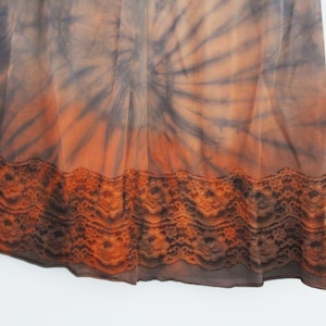 May include: A tie-dye patterned skirt in shades of orange, brown, and gray. The skirt features a lace trim at the hem. The fabric appears to be lightweight and flowing.