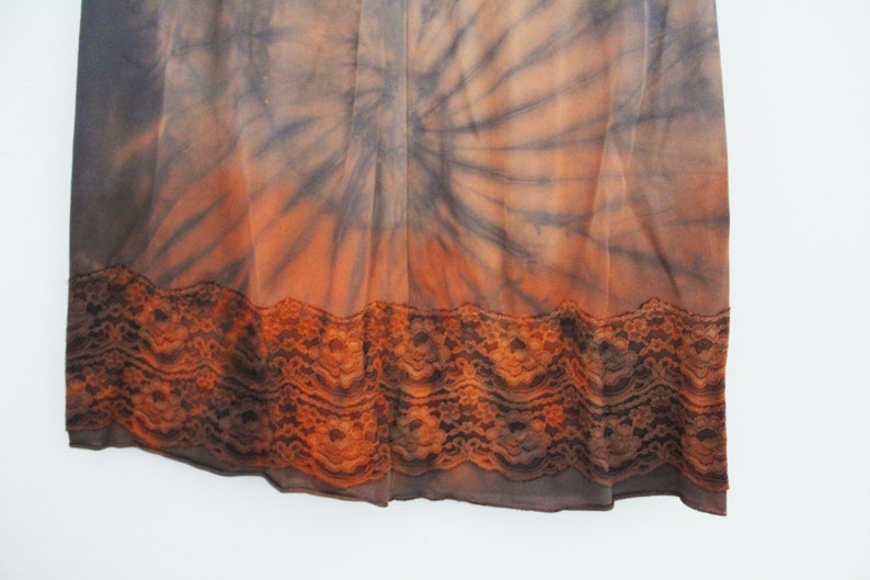 May include: A tie-dye patterned skirt in shades of orange, brown, and gray. The skirt features a lace trim at the hem. The fabric appears to be lightweight and flowing.