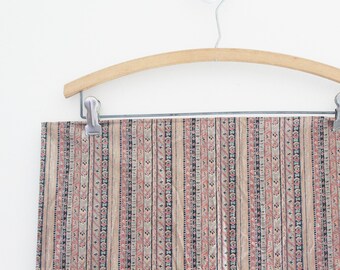 May include: A section of fabric with a vertical striped pattern in beige, red, and navy blue, hanging from a wooden hanger. The fabric's design includes floral and geometric elements.
