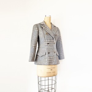May include: A gray and brown houndstooth patterned blazer with a double breasted closure and a single flap pocket on each side.