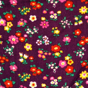 May include: Purple fabric with a repeating pattern of small, colorful flowers. The flowers are in shades of pink, red, yellow, and white.