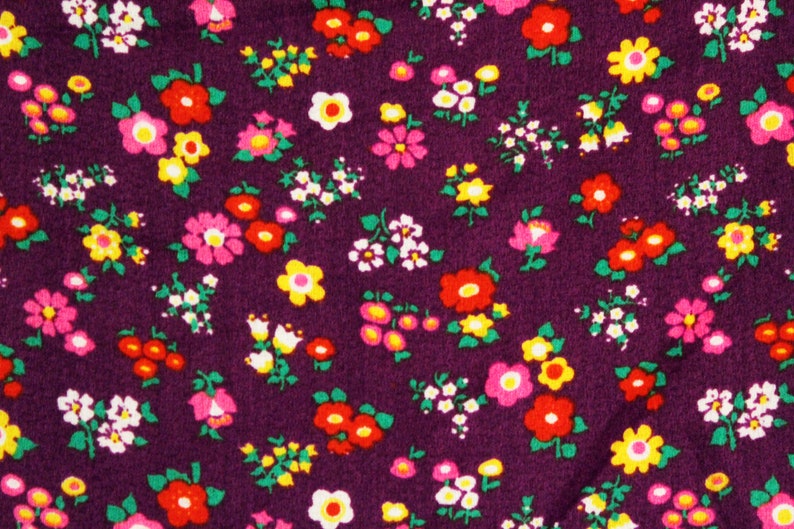 May include: Purple fabric with a repeating pattern of small, colorful flowers. The flowers are in shades of pink, red, yellow, and white.